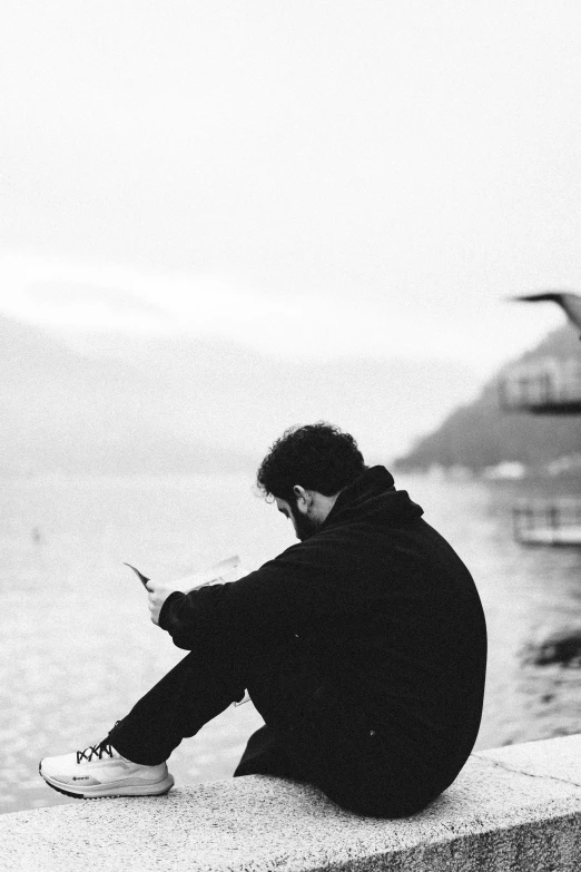 a man sitting down on the edge of a wall with his cellphone