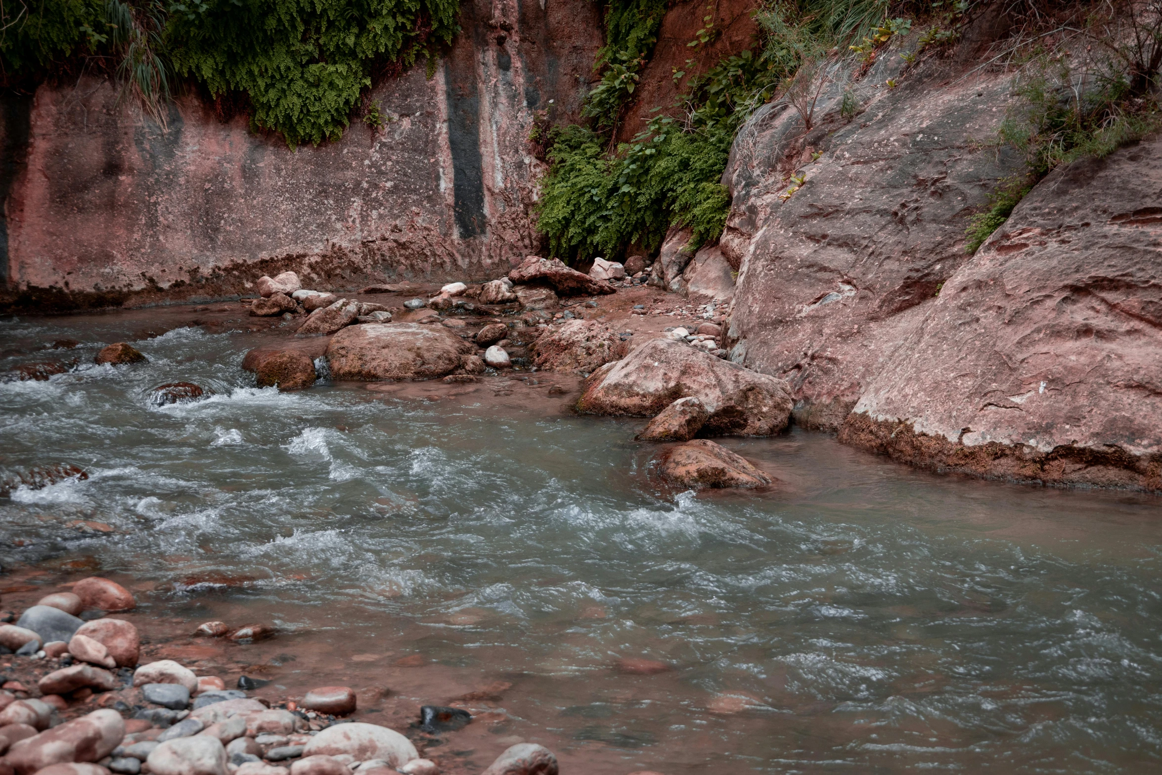 a creek next to a mountain side with lots of rocks