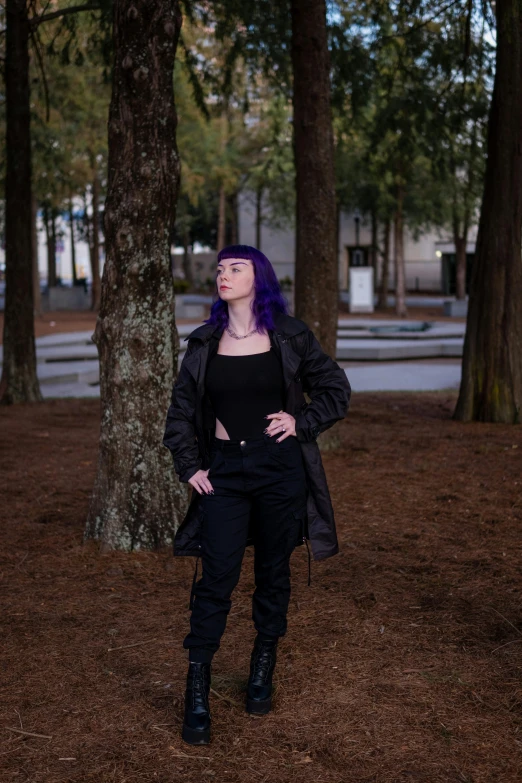 a woman wearing a black coat and black pants standing in the woods