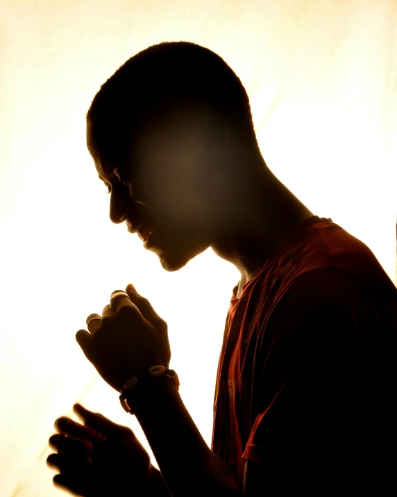 a man in silhouette is praying with his hands clasped