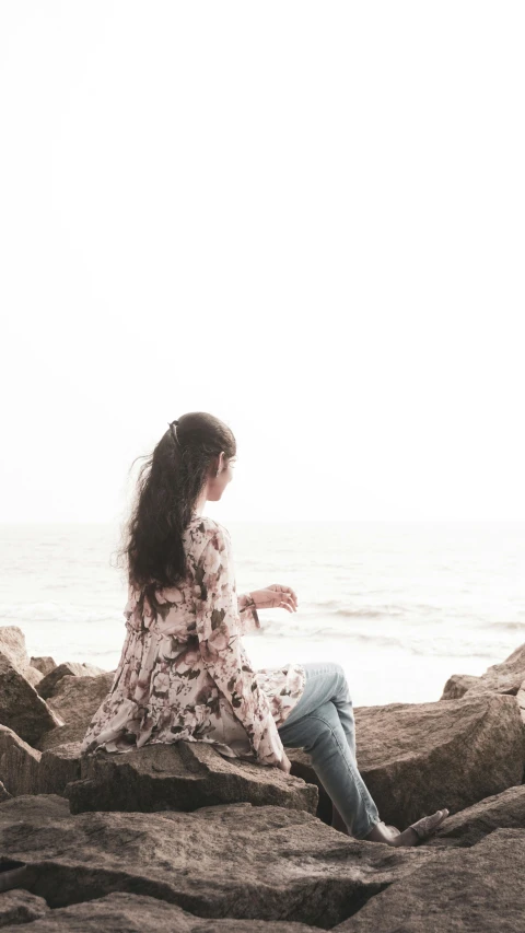 a young lady in floral print top sitting on a rock by the sea