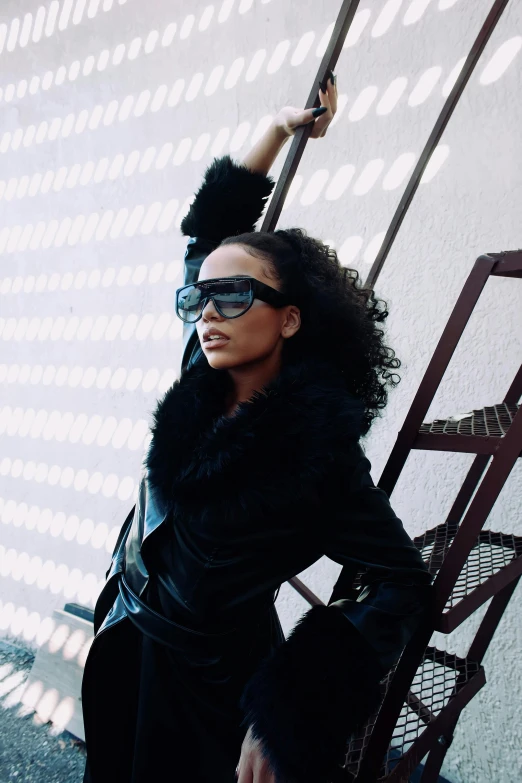 woman in dark colored dress and shades leaning against a fence