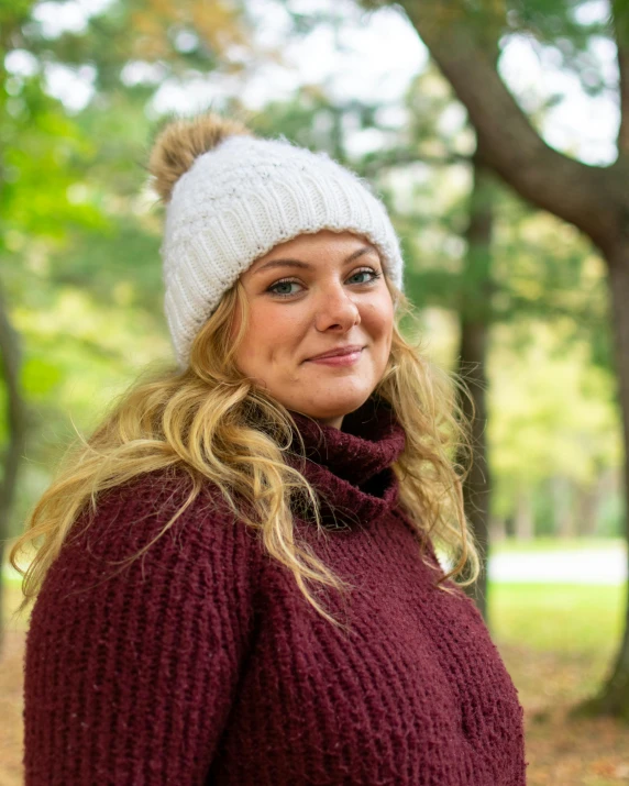 a woman in a maroon sweater and white beanie is smiling