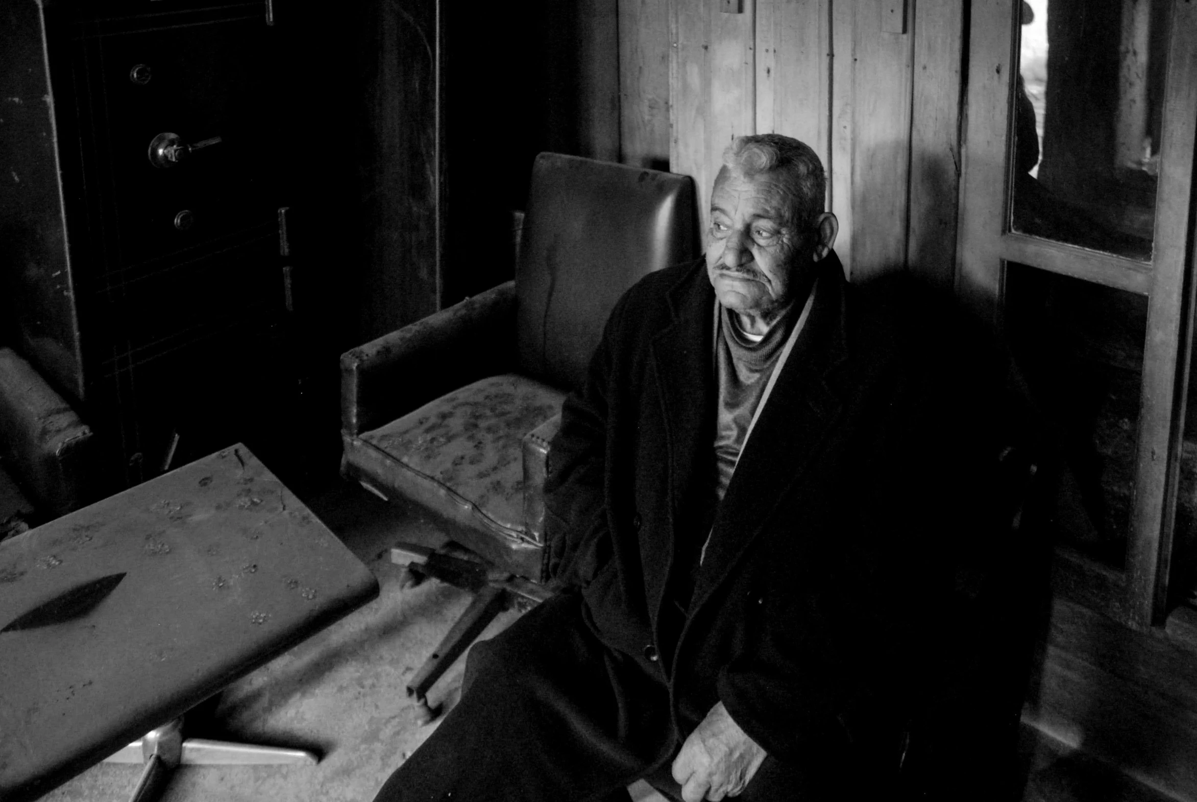 the older man sits in the chair near his home