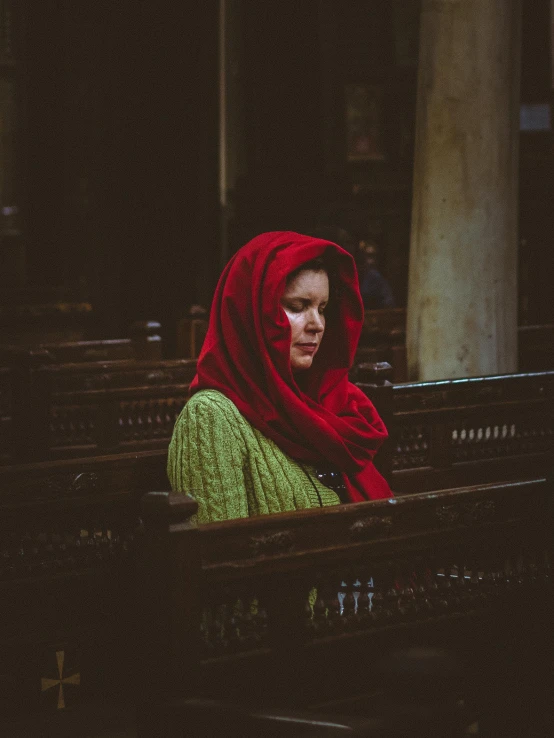 a woman sitting in a church pew alone with red shawl on