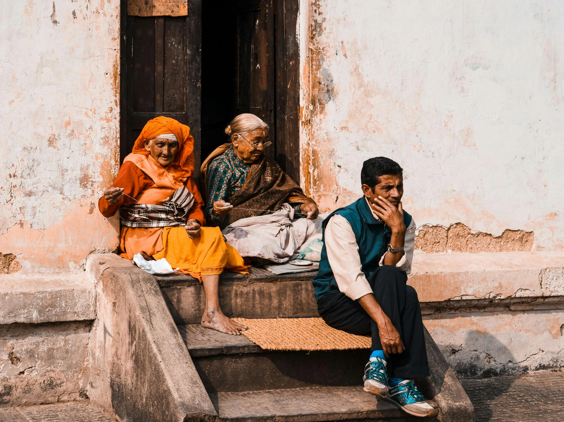 three people sitting on steps near a white building