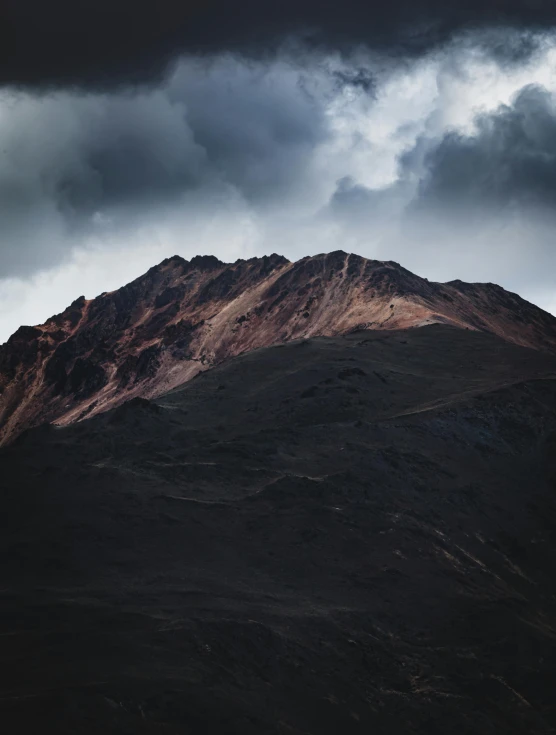 a mountain side with dark clouds in the sky