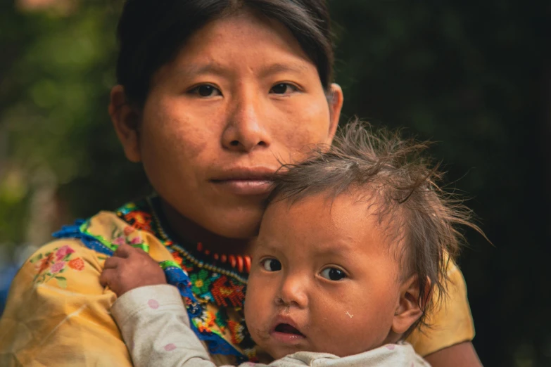 a woman holding a baby who is looking at the camera