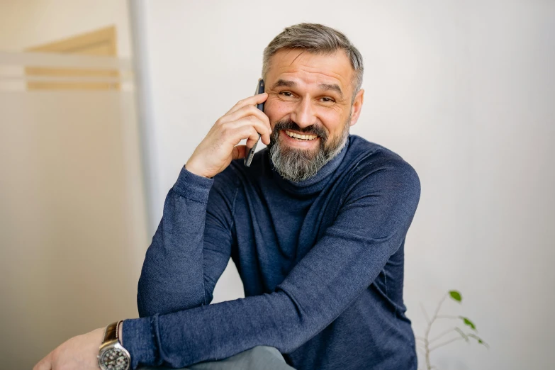 man with gray hair and beard sitting with hand on a head