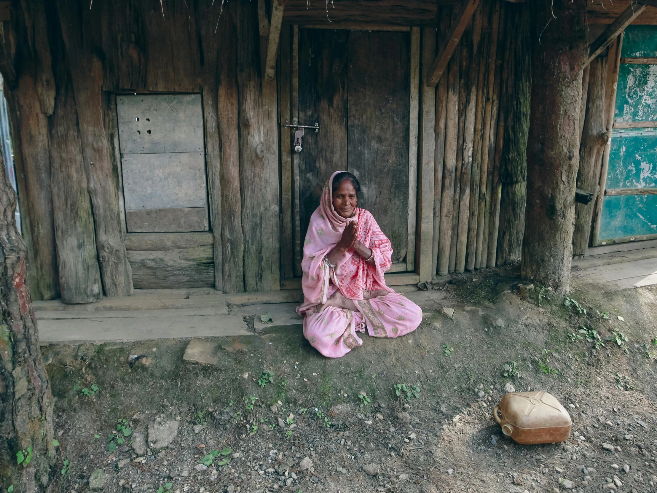 a woman kneeling in front of a wooden structure with doors and a cat on the ground