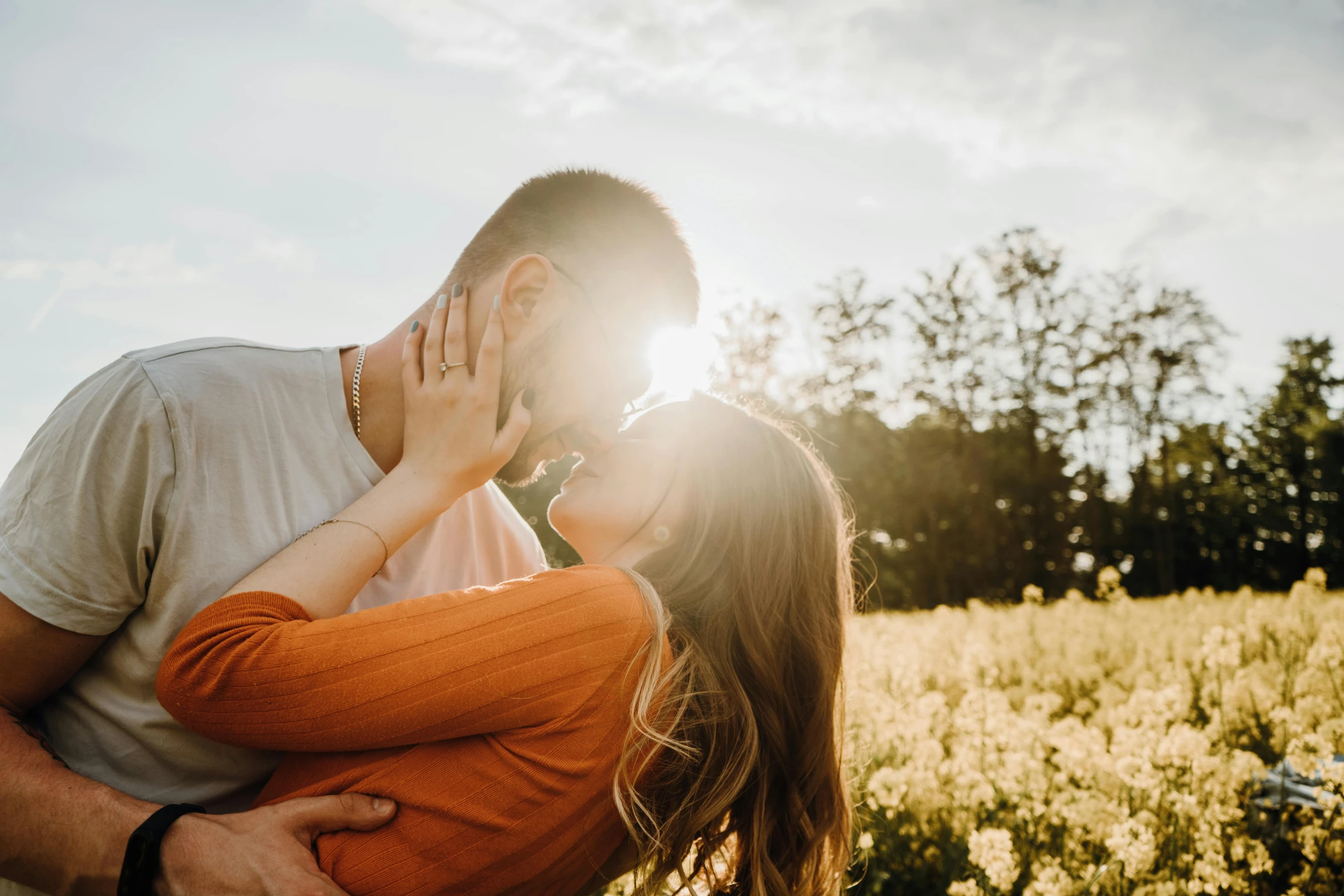 a man kisses the forehead of a woman with the sun shining behind her