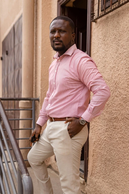 a man in pink shirt and khaki pants leaning up against a balcony