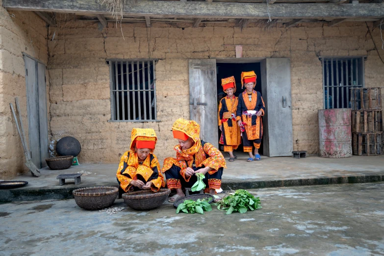 two women wearing bright orange dresses are kneeling down in front of a house
