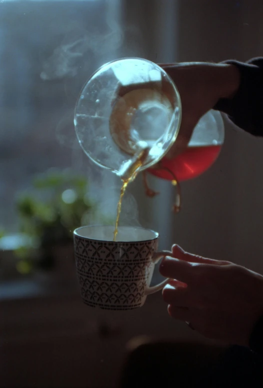 person pouring coffee into a cup, with a light shining on them