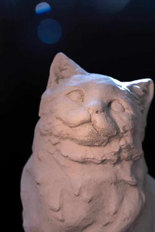 a white cat statue that is next to a black background