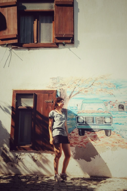 a woman stands against the wall next to a car that is painted