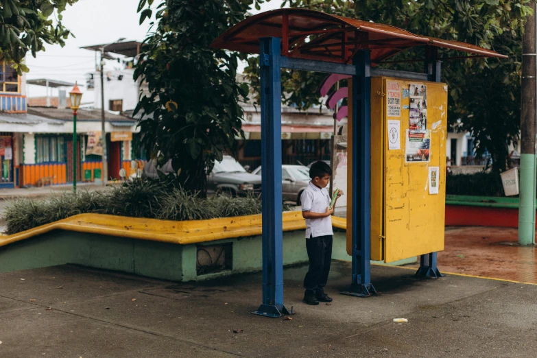 the boy is at a park area next to a yellow vending machine