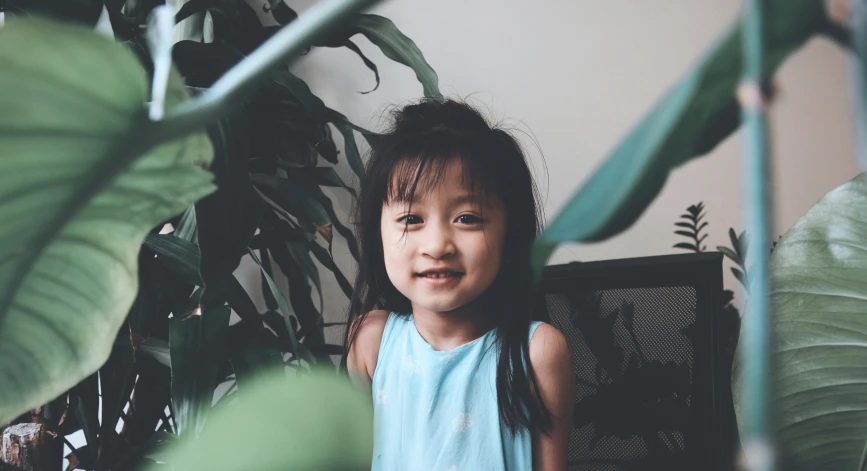 a little girl sitting in front of a green plant