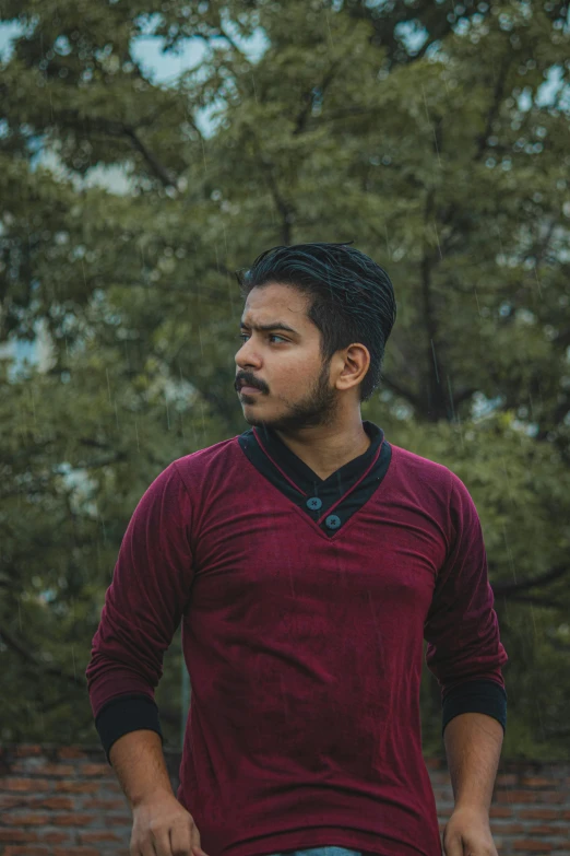 a man wearing a maroon shirt has his hand on his hip and is staring at soing