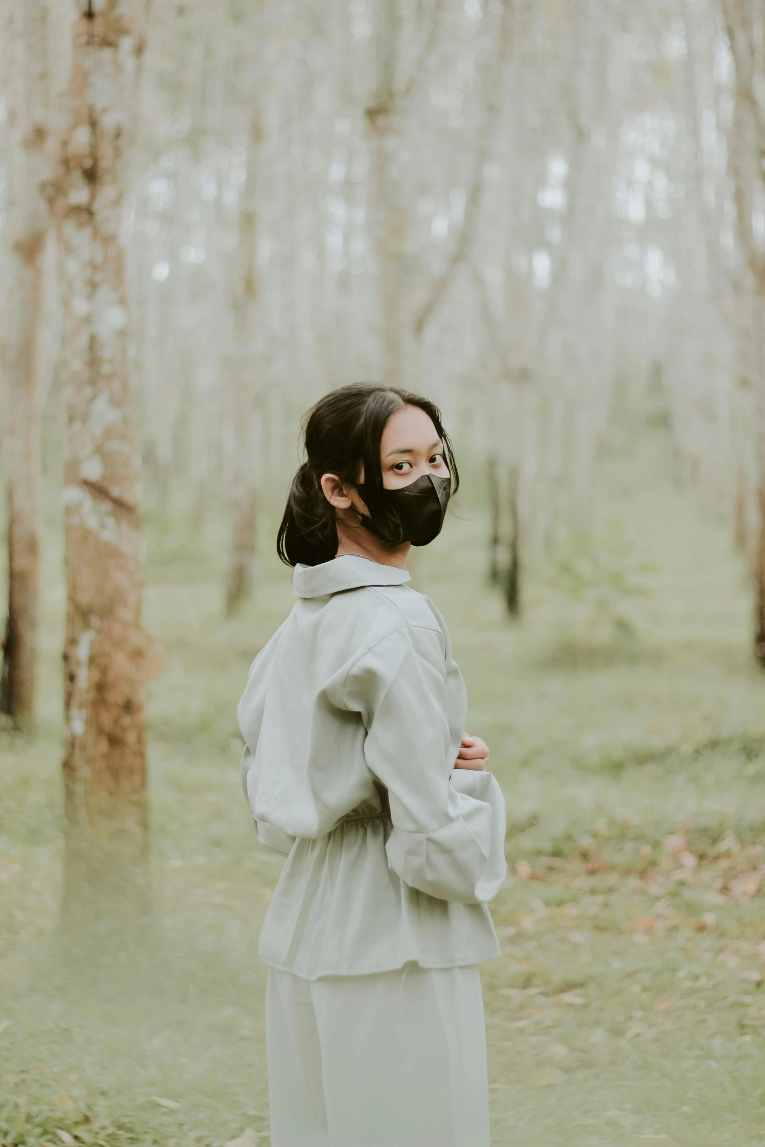 a woman wearing a mask standing in a forest