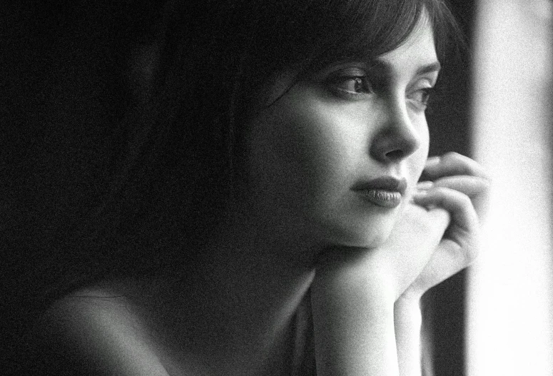 a black and white pograph of a woman looking out the window