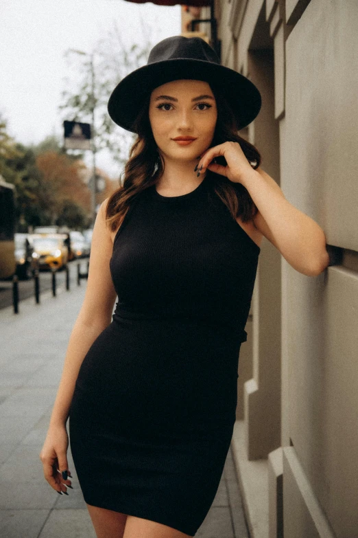 a woman with a black hat leaning on a wall