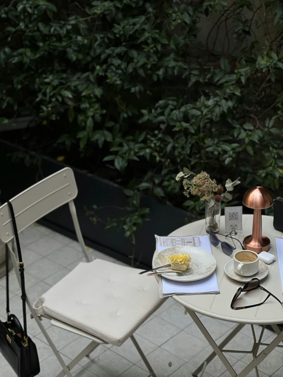 an outdoor set of tables with white chairs and a black purse and book