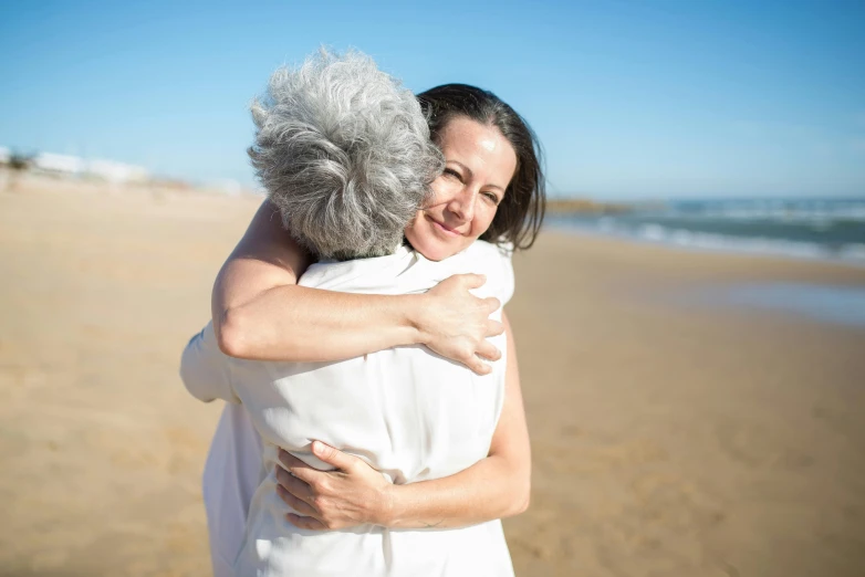 woman hugging older woman on the beach with ocean in background