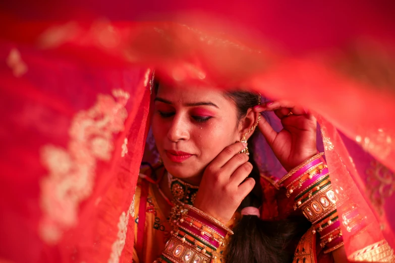 a woman wearing a veil and jewelry standing by some red fabric