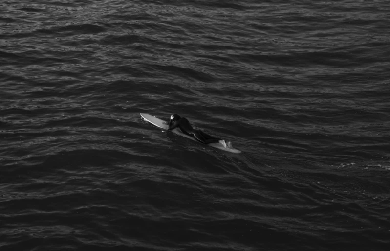 black and white po of a single person sitting on a surf board in the water