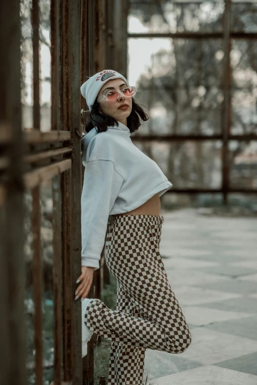 a woman in checkered pants and a beanie leaning against an iron cage