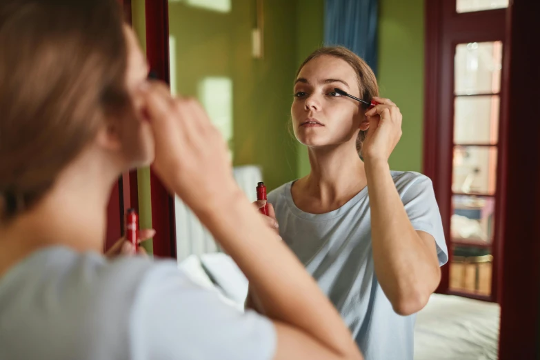 young woman holding a combing tool to her hair in front of the mirror