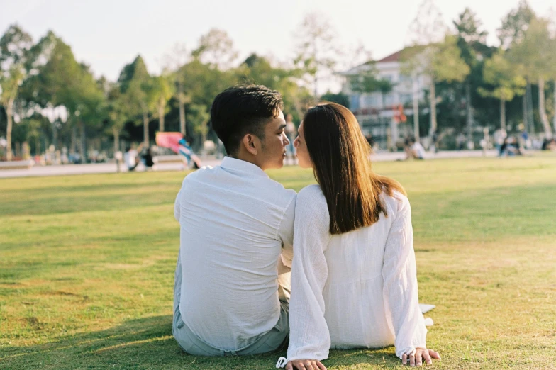 a man and a woman sitting on grass looking at each other
