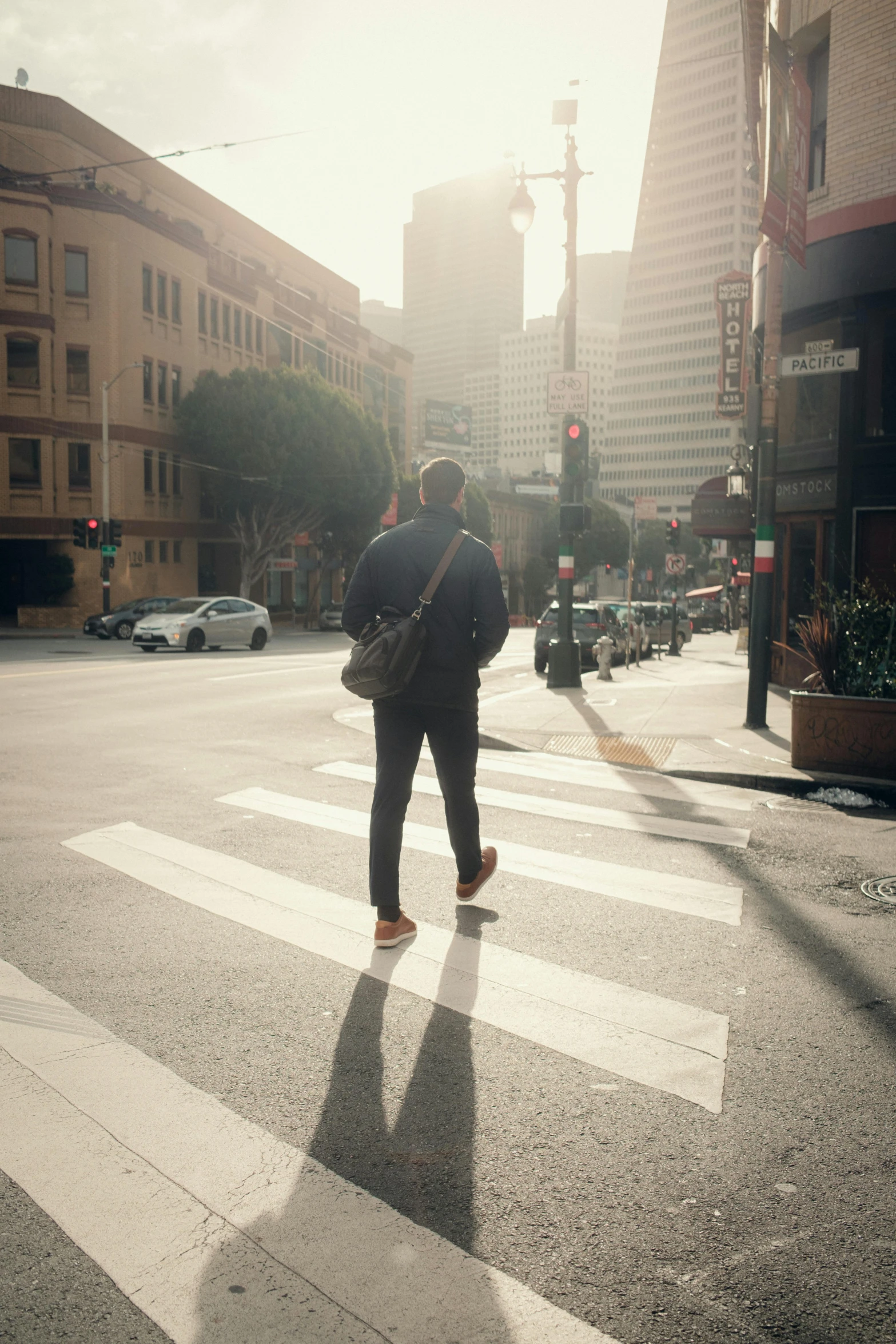 a man standing on a cross walk with a bag over his shoulder