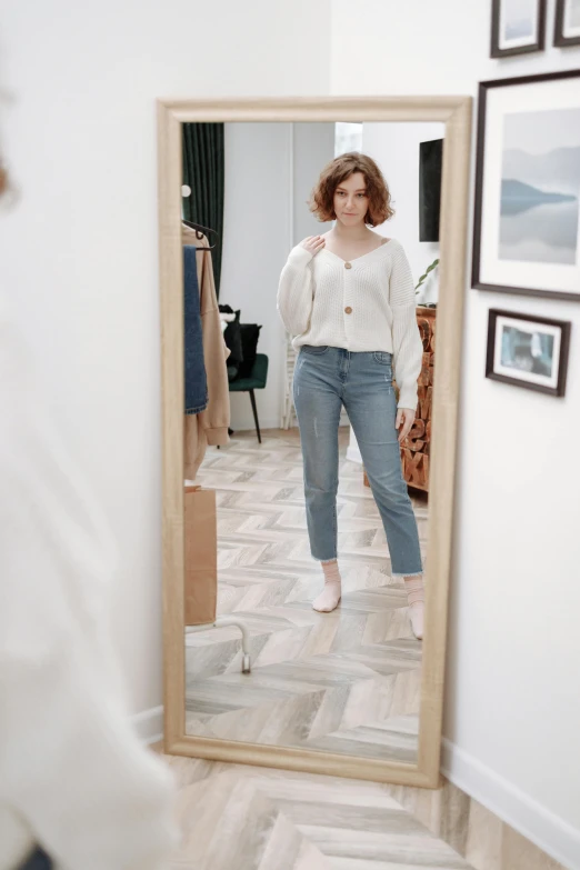 a woman in an open white top looks at herself in a mirror