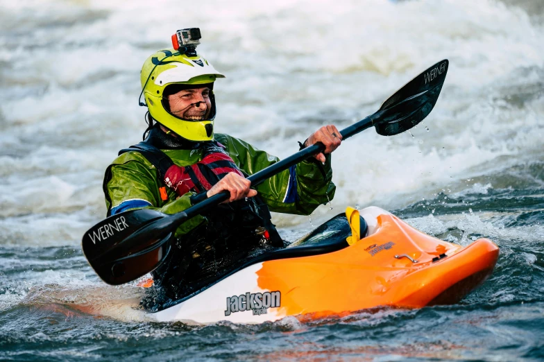 man in helmet and jacket paddling kayak on body of water