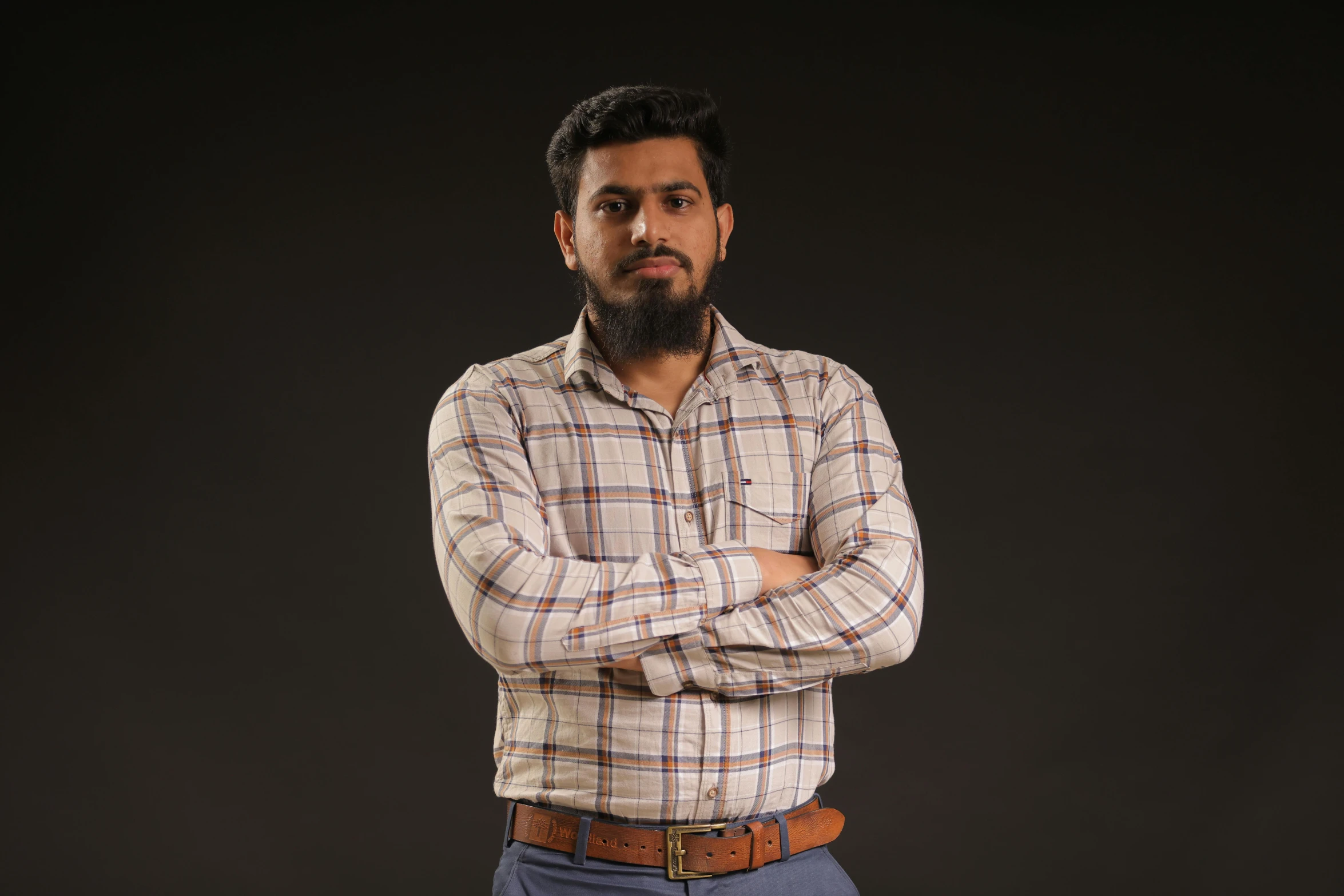 a bearded man in plaid shirt standing with his arms crossed