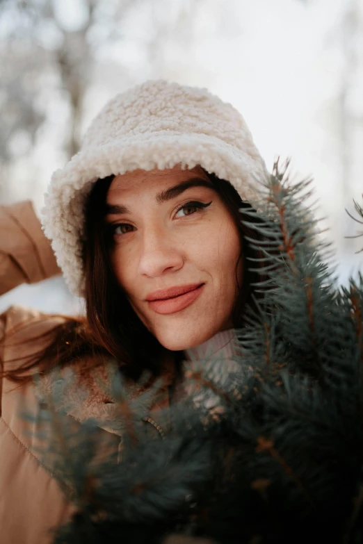 a smiling woman is standing by a fir tree