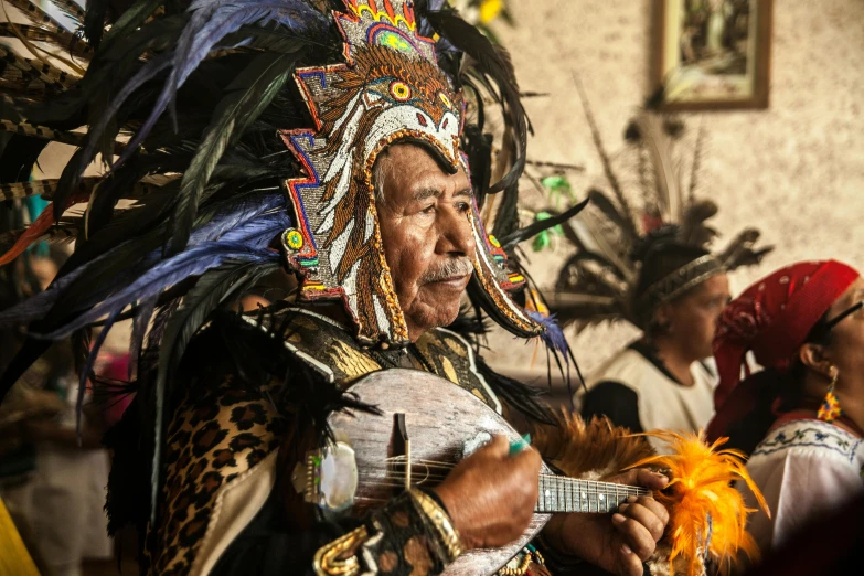 a native american indian plays a guitar while wearing an elaborate headdress