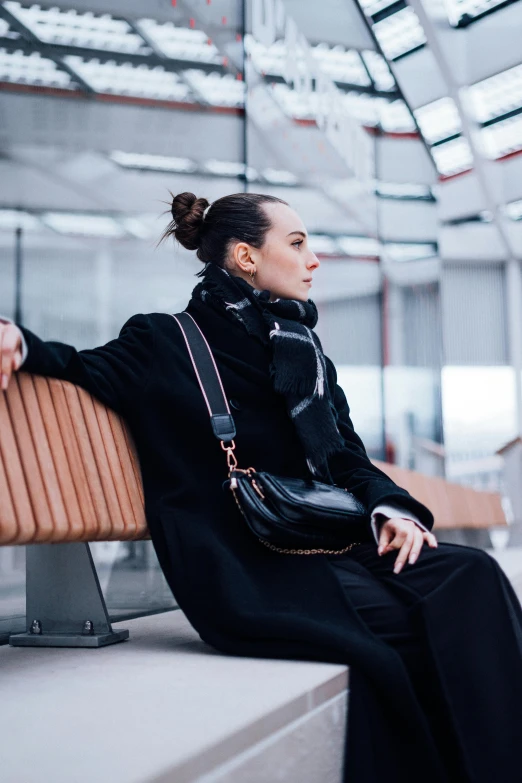 a woman sitting on a bench wearing a black coat