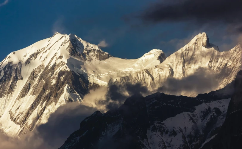 snow covered mountains under cloudy skies, in the evening