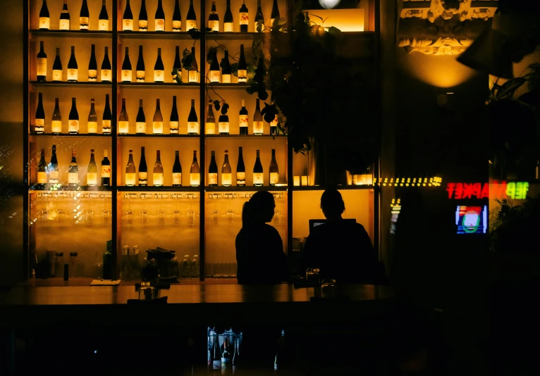 two people sitting at a bar with some bottles