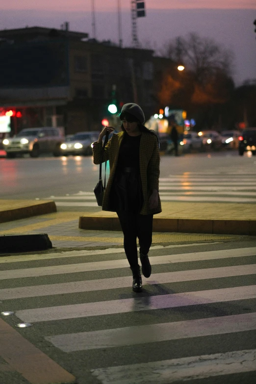 a woman walking across a street at dusk