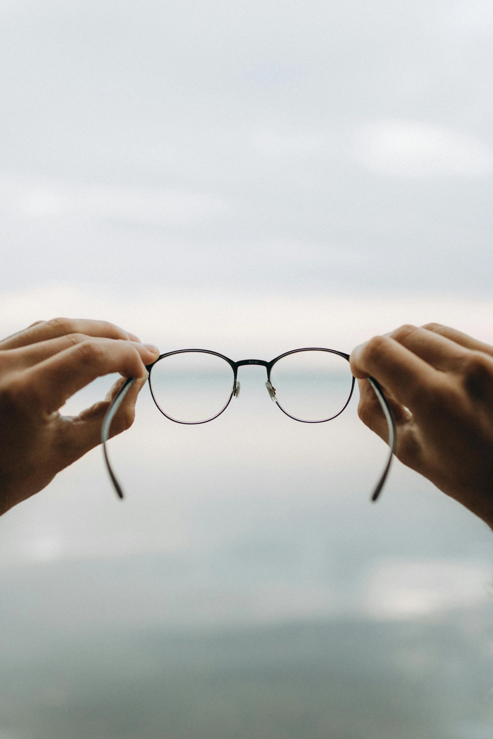 a pair of hands holding up a pair of glasses to the sky