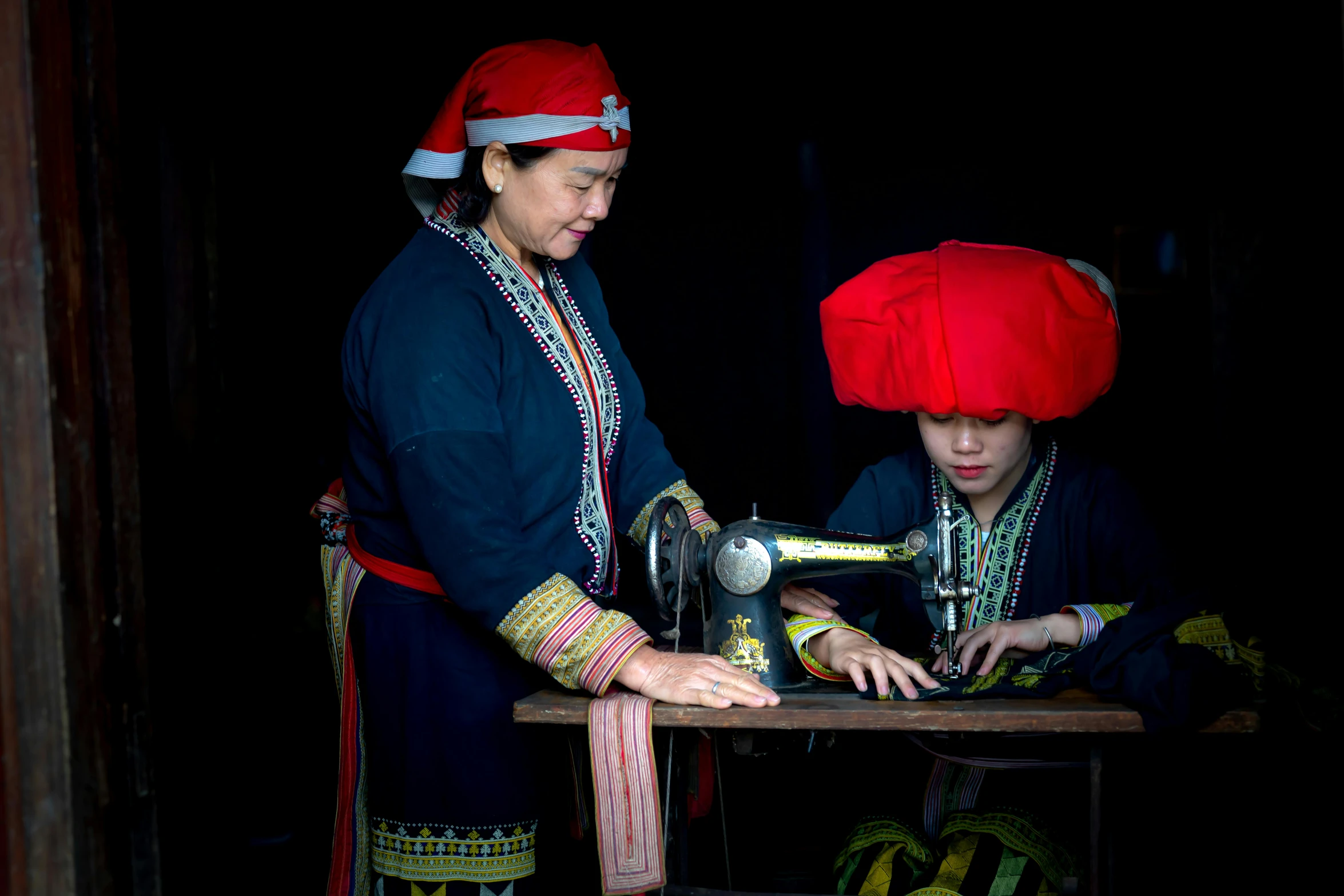 two woman are standing around an old sewing machine