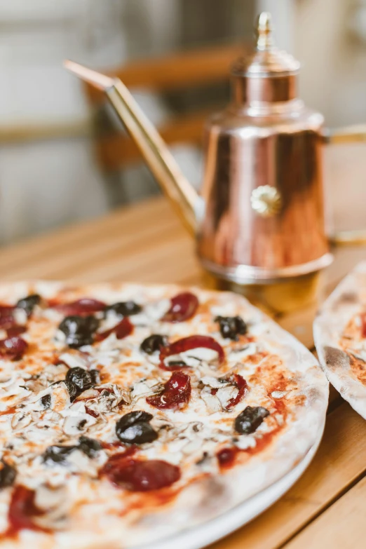 two pizzas with a metallic teapot sitting behind them