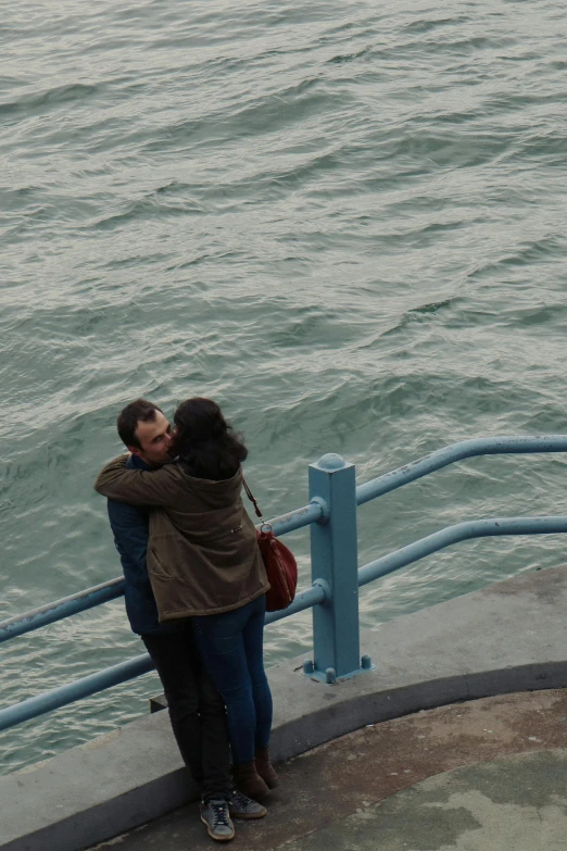 two people hugging each other on a dock overlooking water