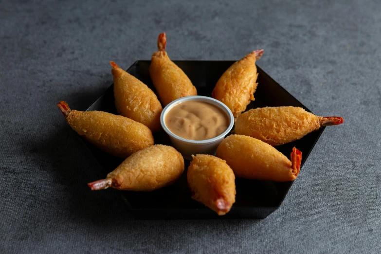 several fish fingers on a black plate with a small bowl in it