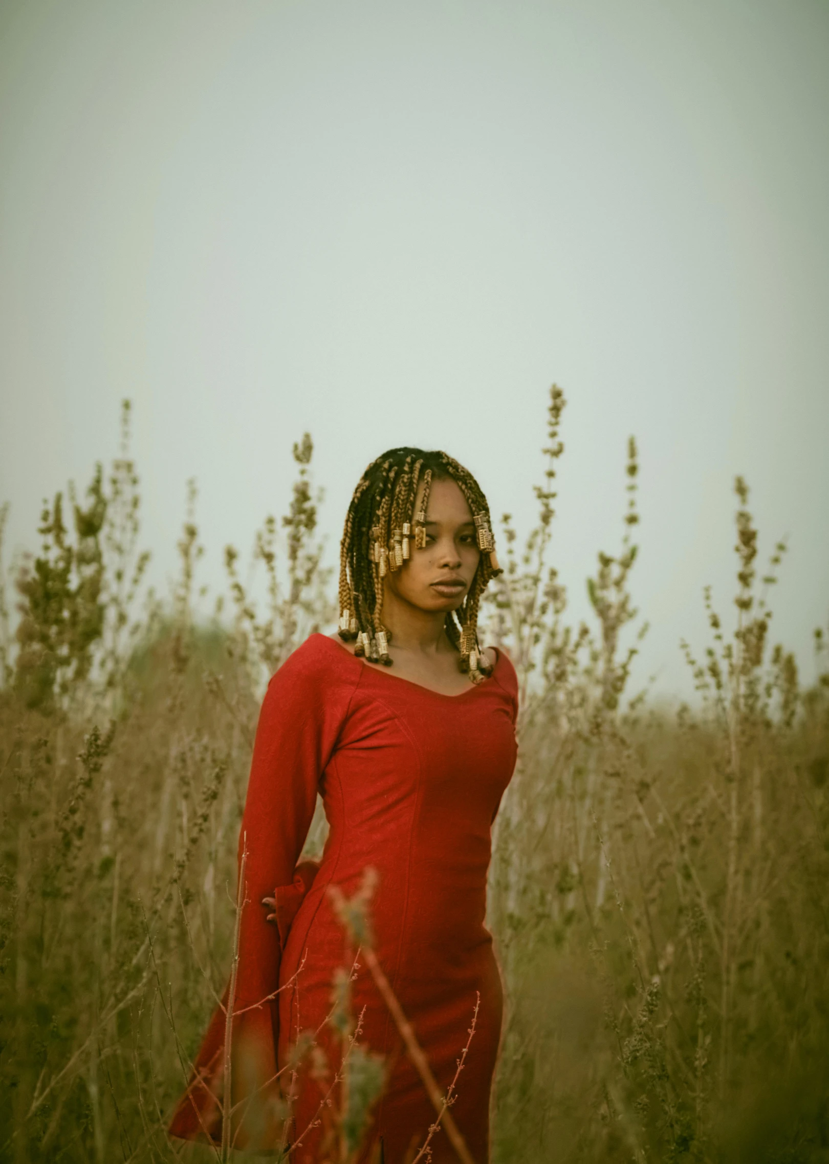 a black woman in red is standing in tall grass