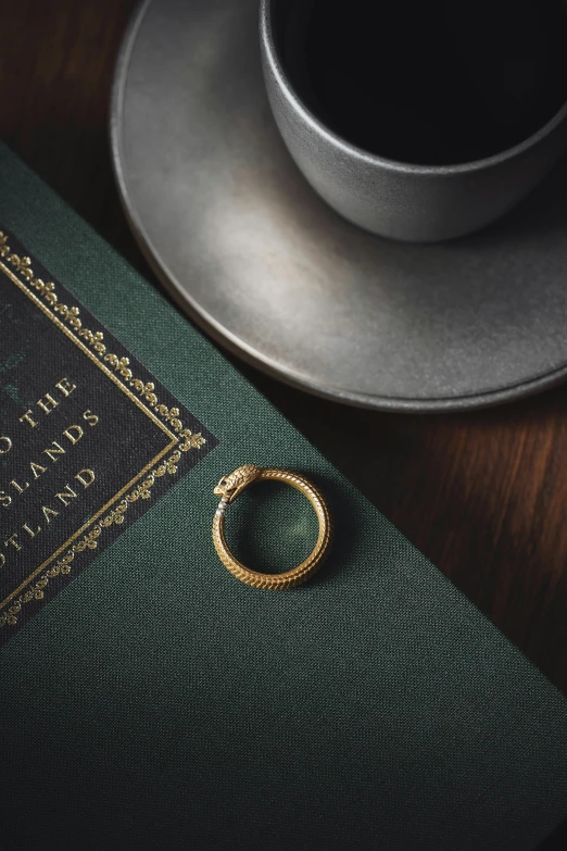 a book, a cup and two rings sit on a table